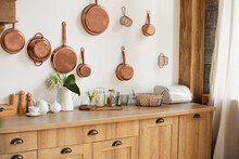 Different Kind Of Cookware And Ceramic Plates On Tabletop Wooden Kitchen. Set Of Copper Saucepans, Pans, Pots And Ladle Hanging In Kitchen. Hanging Kitchen Utensil On Wall. Kitchen Interior Decor	
