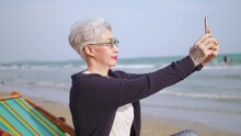 Asian Elderly Woman Taking A Selfie While Relaxing At The Beach.
