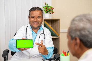 happy smiling doctor at hospital shownig green screen mobile phone to patient - concept of app promotion, advertisement and online appointment