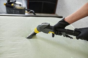 Cleaning service company employee removing dirt from furniture in flat with professional equipment. Female housekeeper arm cleaning the mattress on the bed with washing vacuum cleaner close up