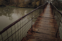 Eerie Scenery Of A Wooden Suspension Bridge Over The River In A Cloudy Day