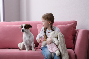 Wall Mural - Cute little girl with her dog and toy bunny on sofa indoors. Childhood pet