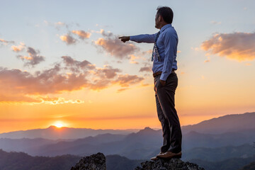 Wall Mural - Successful businessman in business suit standing and looking sunset on top rock mountain background,  competition and leadership concept.