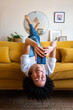 © Daniel - Happy African American woman lying upside down on the couch texting using mobile phone. Checking social media. Vertical.
