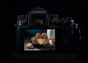 Wall Mural - DSLR camera or mirrorless body lit by a rim light showing sweet bread and milk on the back of the camera display. Low key light photography