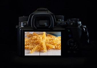 DSLR camera or mirrorless body lit by a rim light showing raw pasta on the back of the camera display. Low key light photography