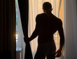 © Volodymyr - Sexy gay silhouette. Man undresses. Young guy with beautiful bare naked torso. Sexy young muscular man on window at morning, back light.