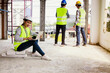 © ฺฺฺBoonterm - Architect businessman beautiful asian woman wearing helmet and yellow vest sits with laptop examining construction site reports two male workers standing behind building's construction site consulting