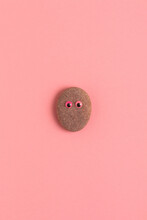 Oval Shaped Stone With Decorative Eyes On A Pink Background.