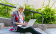 © MARALEM - El teletrabajo en la nueva normalidad , mujer de negocios trabajando en cualquier parte del mundo, mujer sentada en las escaleras de un parque teletrabajando con su computadora portátil