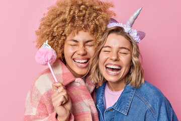 Wall Mural - Happy joyful young women have fun laugh gladfully keep eyes closed smile toothily dressed in fashionable jackets isolated over pink background. Positive human emotions and friendship concept