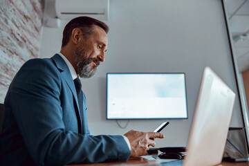 side view of smiling bearded man busy while reading message while sitting at desk