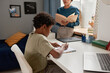 © Mediaphotos - Concentrated African American boy with curly hair sitting at desk and preparing for dictation with tutor