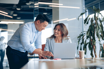 Wall Mural - Confident asian office worker discussing work with mature business woman. Blurred background