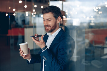 Wall Mural - smiling businessman is using smartphone to record a voice message to her business partner at office