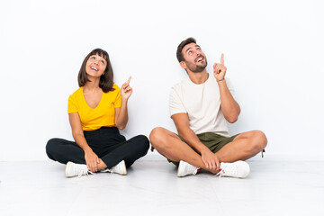 Wall Mural - Young couple sitting on the floor isolated on white background pointing a great idea and looking up