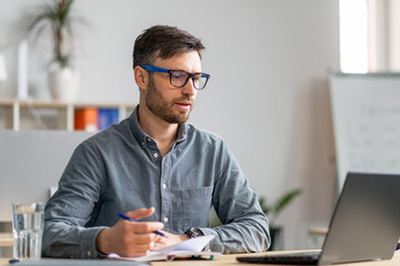 Poster - Successful middle aged businessman working at office, sitting at workdesk in front of laptop and taking notes