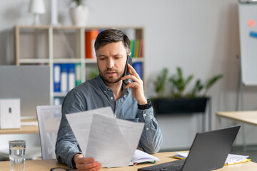 Poster - Handsome mature male manager sitting at office, reading documents and having phone conversation, copy space