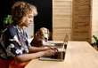 African young girl with curly hair doing online work on laptop together with her animal companion at table