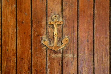 Wall Mural - Close-up of a weathered wooden door decorated with a small rusty anchor