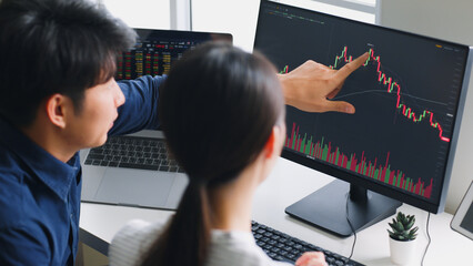 Young Asian investors analyzing about stock market and cryptocurrency investment from graph in computer laptop together.