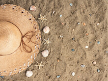Flat Lay Straw Hat On Beach Sand Beside Seashells, Seafish And Small Stones