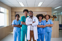Young African American Male Doctor Smiling While Standing In A Hospital  With A Diverse Group Of Staff In The Background