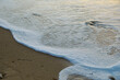 Seichte Welle mit Schaum auf feinem Sandstrand bei Sonnenuntergang