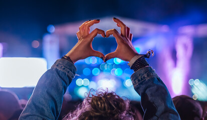 Woman making heart shape with hands at music event 