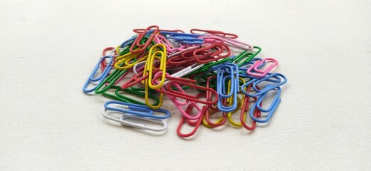 Paper clip pile, bunch, group or collection of multycolored colorful school or office paperclip isolated on white table desk background surface with copy space. Horizontal closeup macro side view.