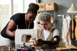 © AnnaStills - Two young creative female specialists in sewing clothes working together in front of electric machine in modern spacious workshop