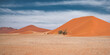 Panorama of a tranquil scene with deep orange sand dunes with light clouds behind 