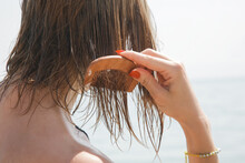 Woman's Hair On The Beach. Woman Applaying Hair Mask With Wooden Comb. Hair Damage Due To Salty Ocean Water And Sun, Summertime Hair Care Concept.	
