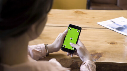 Poster - Woman holding a smartphone in her hands and scrolling the green screen with tracking marks. Stock footage. Female looking at her modern cell phone with chroma key, new technology concept.