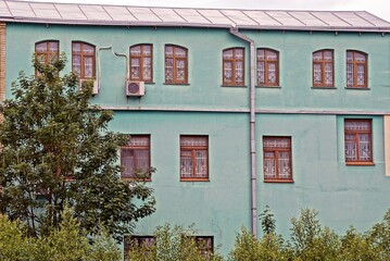 Sticker - facade of a large old green house with a row of brown windows on the street among the vegetation