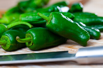 Wall Mural - Whole fresh green padron peppers on wooden table with knife. Vitamin cooking ingredients ..