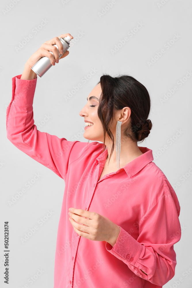 Pretty young woman with hair spray on grey background