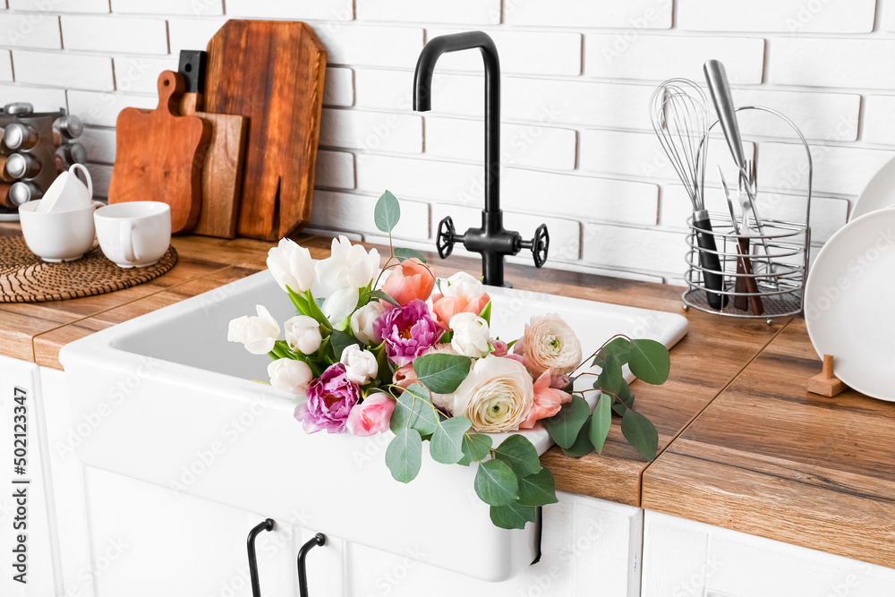 Sink with beautiful flowers and kitchen utensils on counters near white brick wall