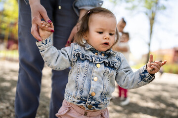 One baby small caucasian child little girl in park with her mother holding hand while assisting to walk in bright spring day real people childhood development learning and family concept copy space