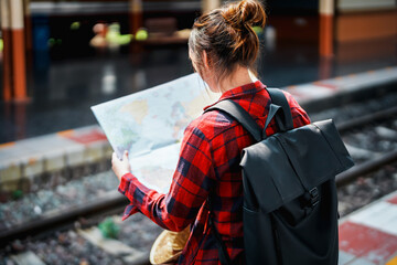 Wall Mural - summer, relax, vacation, travel, portrait of a cute Asian girl looking at a map to plan a trip while waiting at the train station.