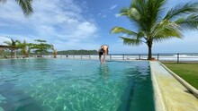 SLOW MOTION: Young Woman Diving In Infinity Pool At Tropical Beach Resort With Oceanview. Female Person Enjoying Summer Days At Exotic Luxury Resort In Panama. Refreshment On A Hot Summer Day.