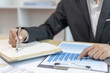 © Puwasit Inyavileart - Head of marketing is recording the company's financial growth statistics using graphs as a reference for reviewing and analyzing the results, Taking notes and analyzing data graphs in office.