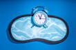 Healthy deep sleep background. Circadian rhythms, circadian clocks and biological clock concept. Blue fabric sleep mask with an alarm clock on dark blue background. Simple flatlay copy space
