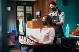 Hairstylist and her customer choosing hair dye from palette at hair salon during coronavirus pandemic.