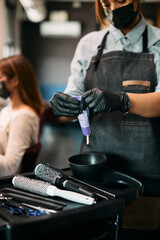 Close-up of hairdresser squeezing hair color from tube at hair salon.