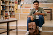 © Drazen - Happy black student using mobile phone at university library and looking at camera.
