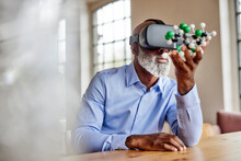 Mature Scientist With Virtual Reality Simulator Examining Molecular Model At Home