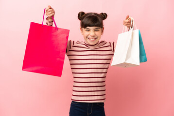 Wall Mural - Little caucasian girl isolated on pink background holding shopping bags and smiling