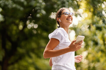 A smiling young woman with eyeglasses is listening to her favorite radio station and walking in nature. 