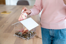 Woman Putting Paper Currency In Piggy Bank At Home